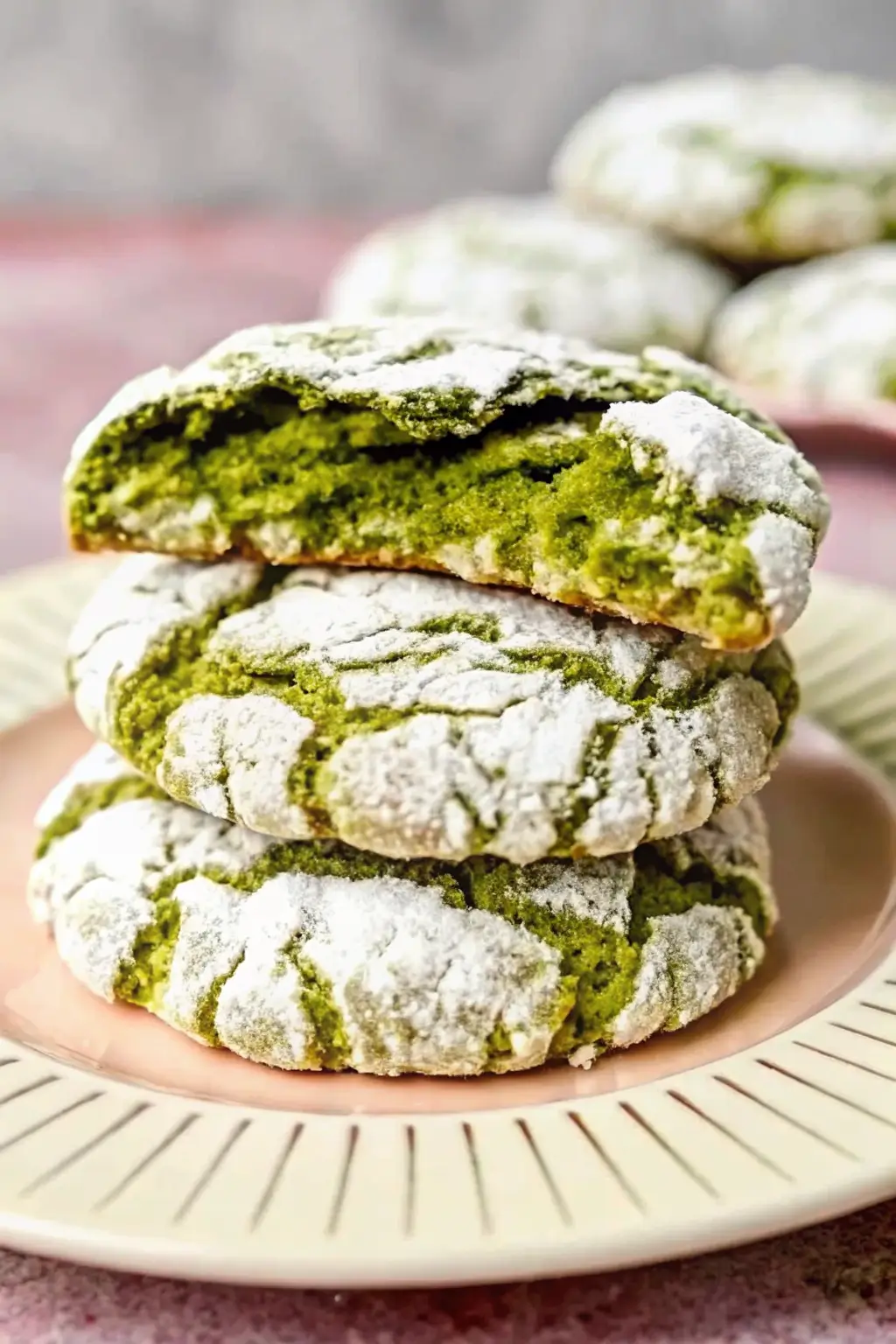 Freshly baked matcha crinkle cookies covered in powdered sugar on a baking tray.