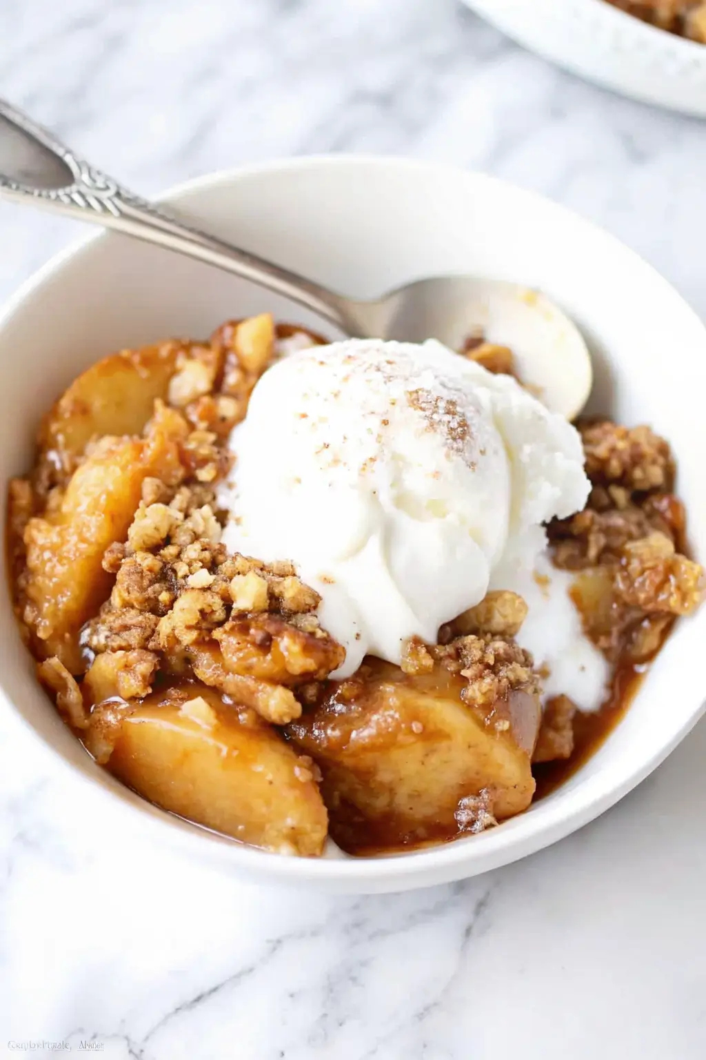 Bowl of freshly baked apple crisp topped with vanilla ice cream and cinnamon