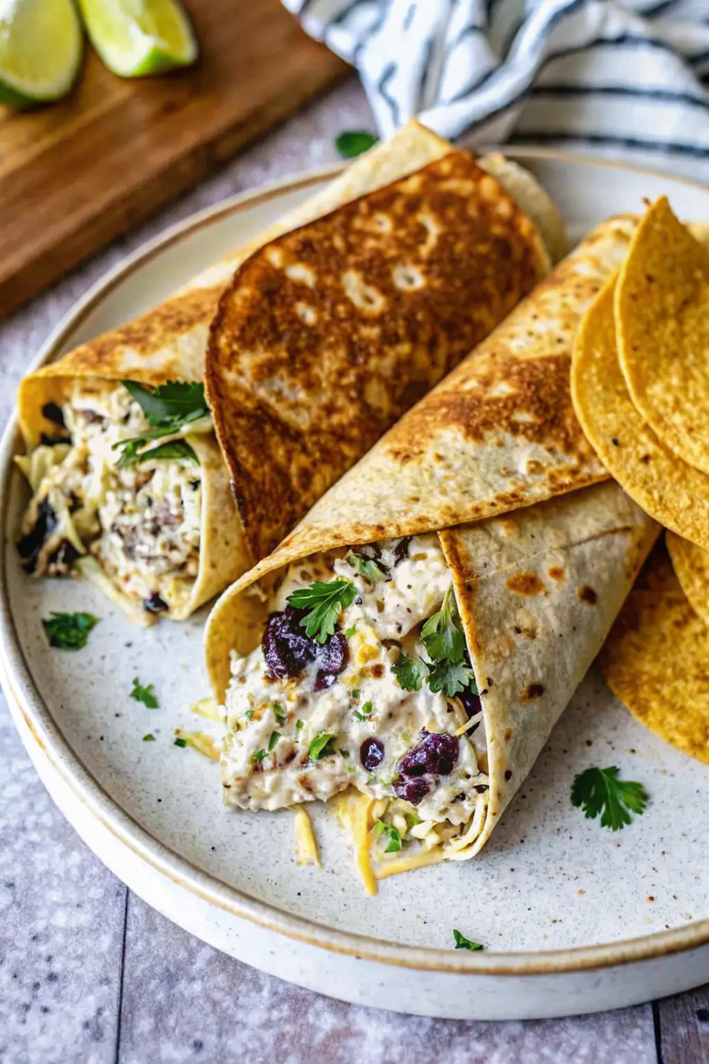 Hands rolling a fresh chicken salad wrap on a cutting board