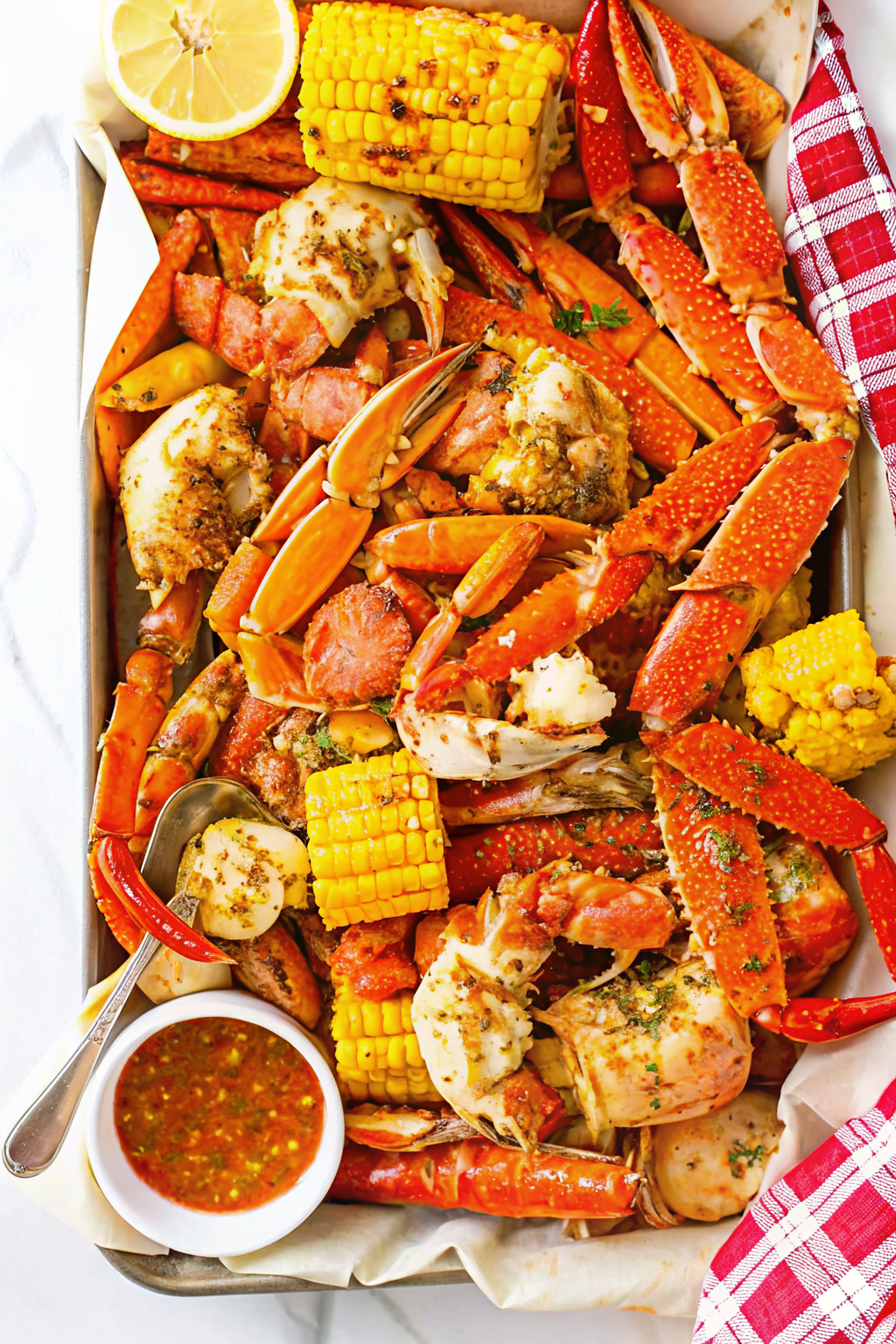 A table covered in newspaper piled high with a seafood feast of crab, shrimp, and corn.