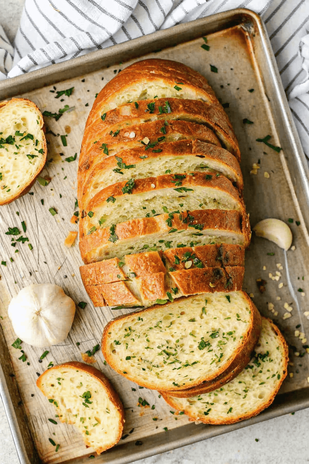Crispy golden garlic bread slices topped with melted butter and fresh parsley on a baking sheet