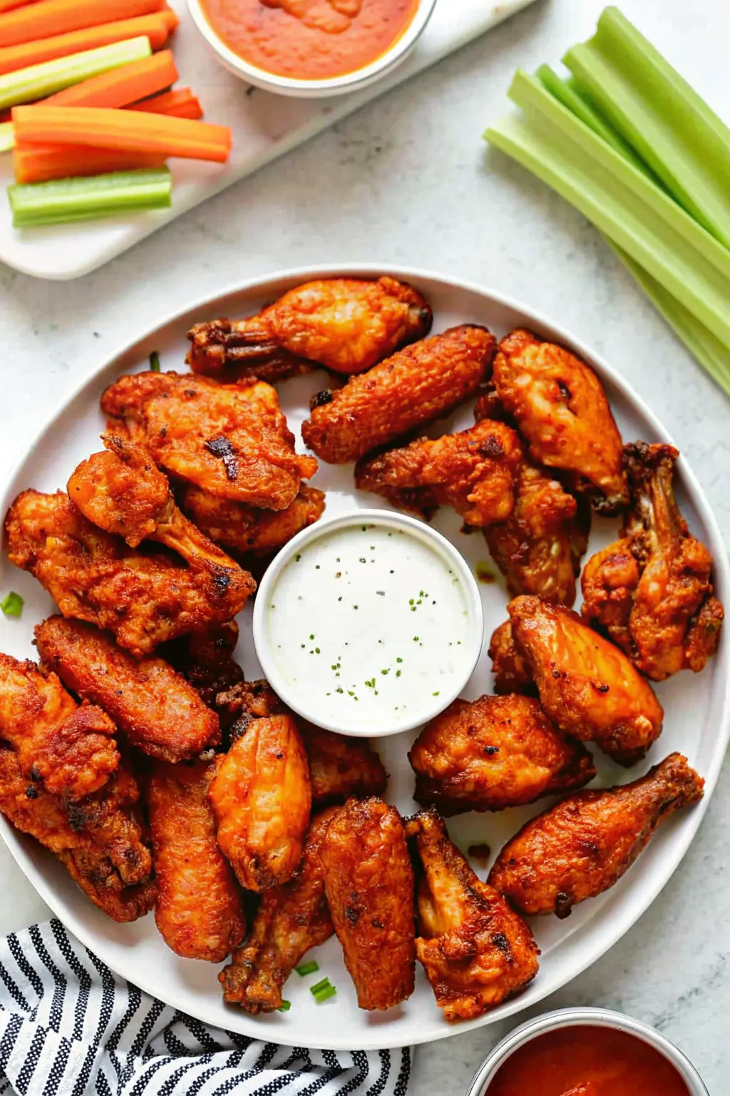 A plate of crispy buffalo chicken wings served with ranch dipping sauce, celery sticks, and carrot sticks.