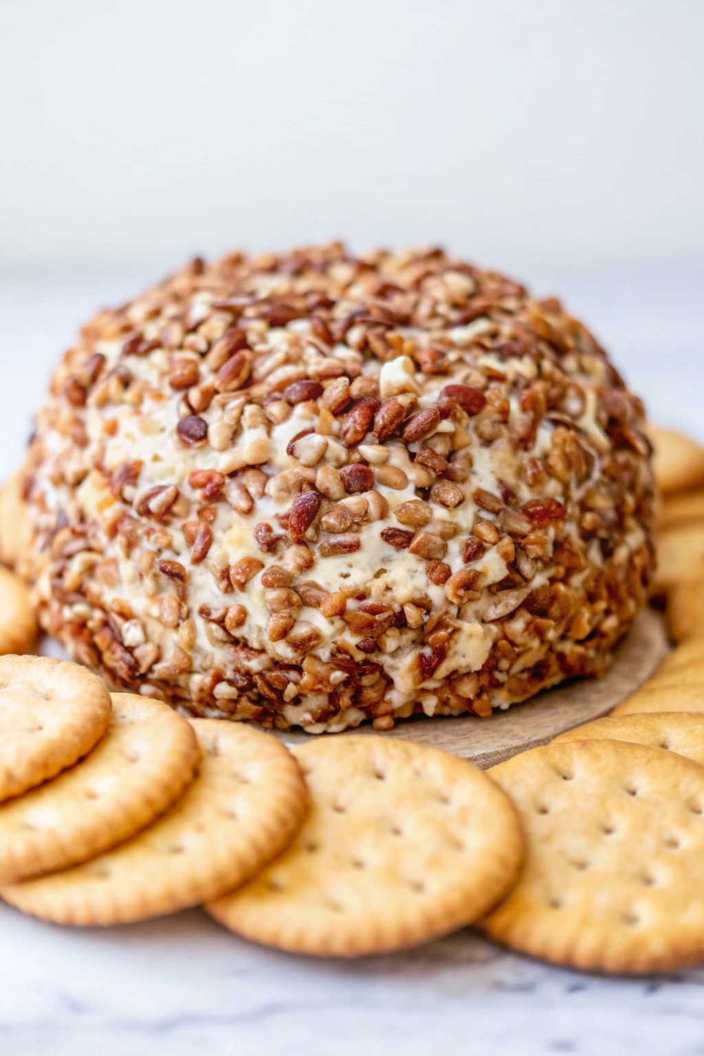 A classic cheese ball coated in chopped pecans served on a wooden board with crackers.