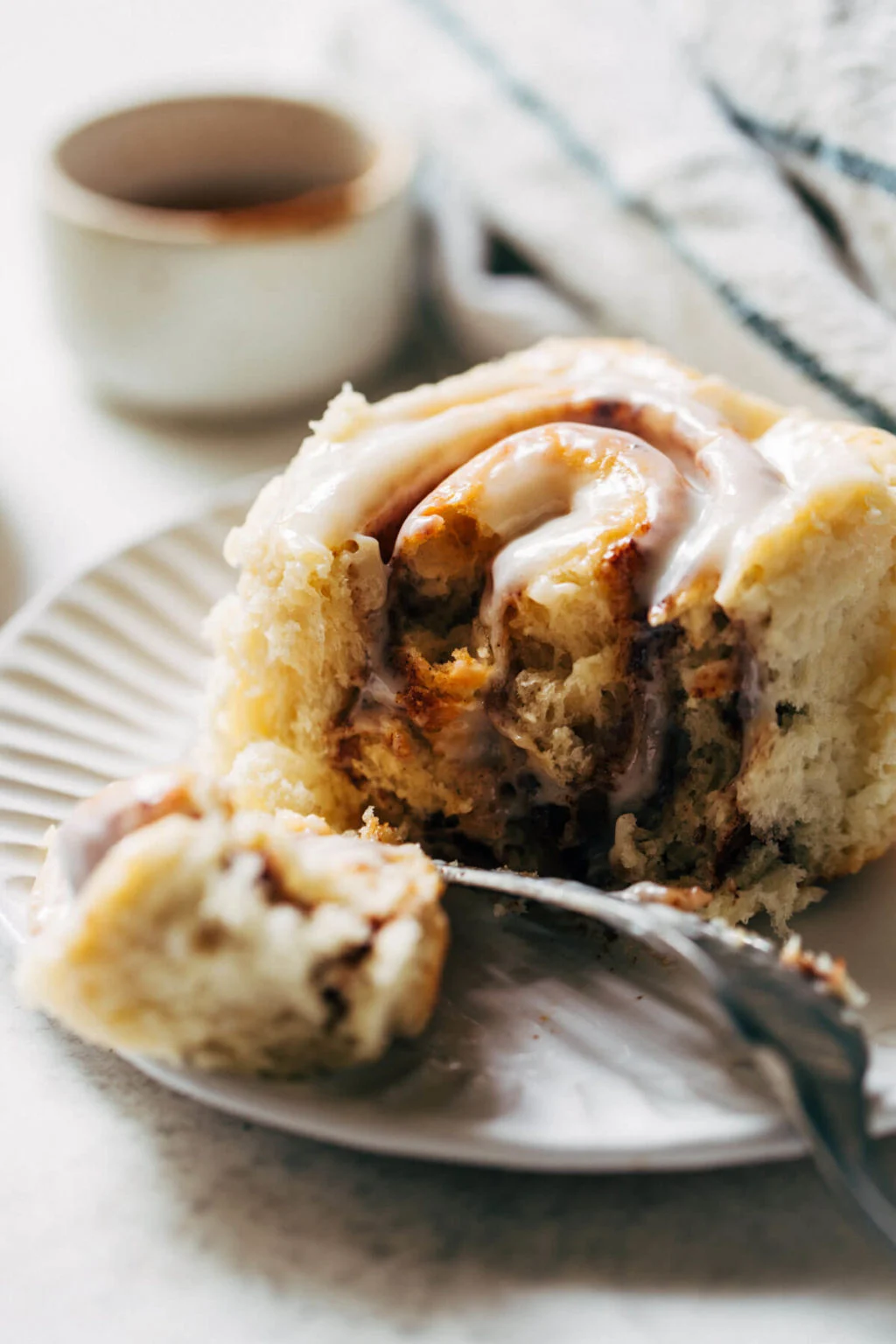 A ceramic pan filled with golden brown cinnamon rolls covered in melting cream cheese frosting.