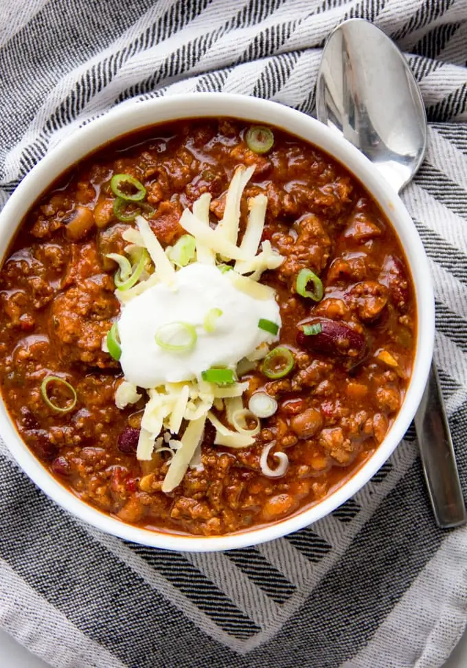 A rustic bowl of American Chili Escoffier with tender beef, beans, and rich tomato sauce, styled on a kitchen towel for a warm homemade look.