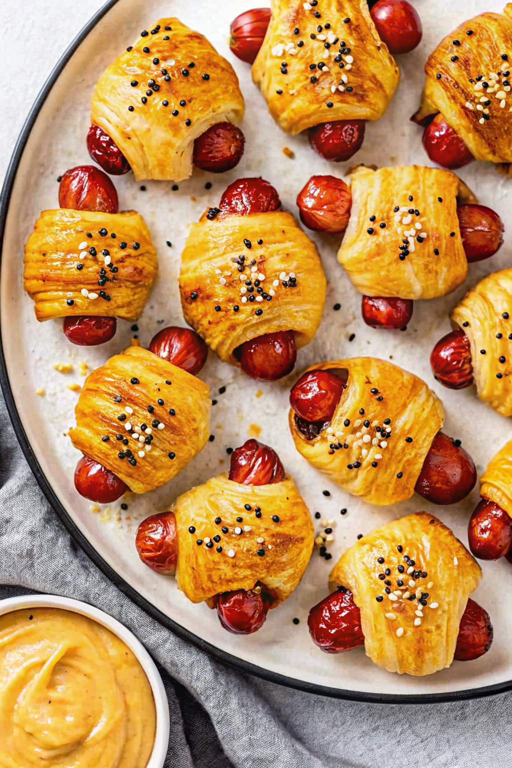 Uncooked crescent dough triangles being rolled around cocktail sausages.