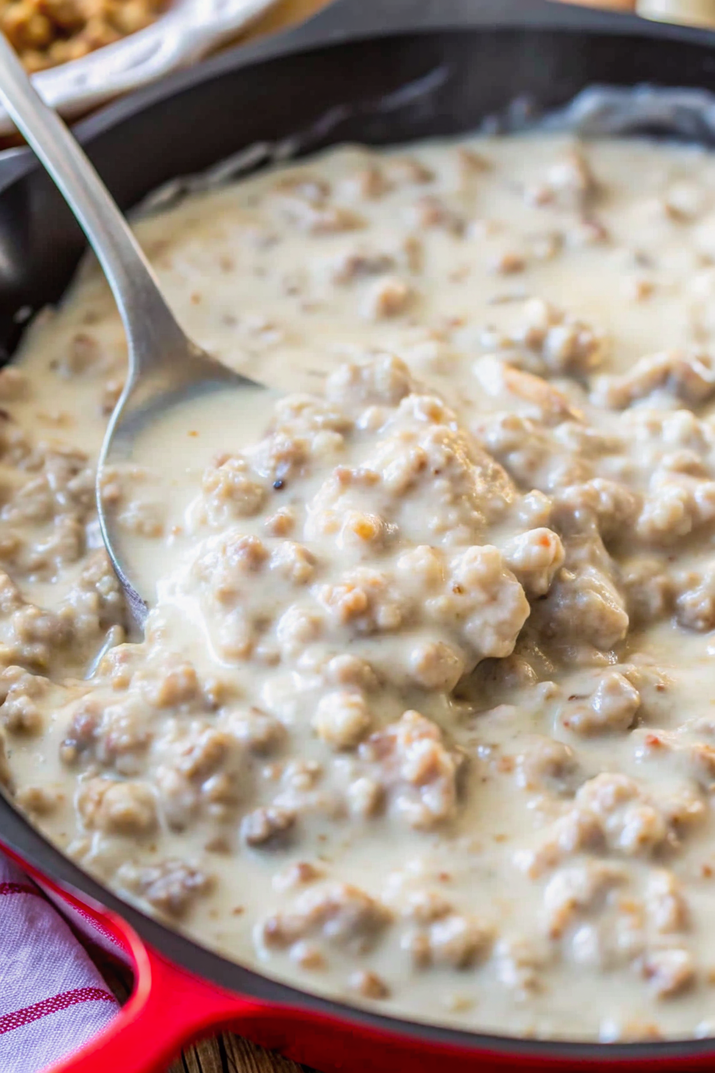 Ground pork sausage browning in a cast iron skillet with a wooden spoon
