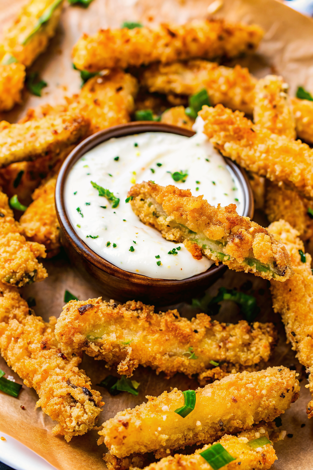 A rustic wooden board stacked with crispy Parmesan crusted zucchini fries and marinara dipping sauce.