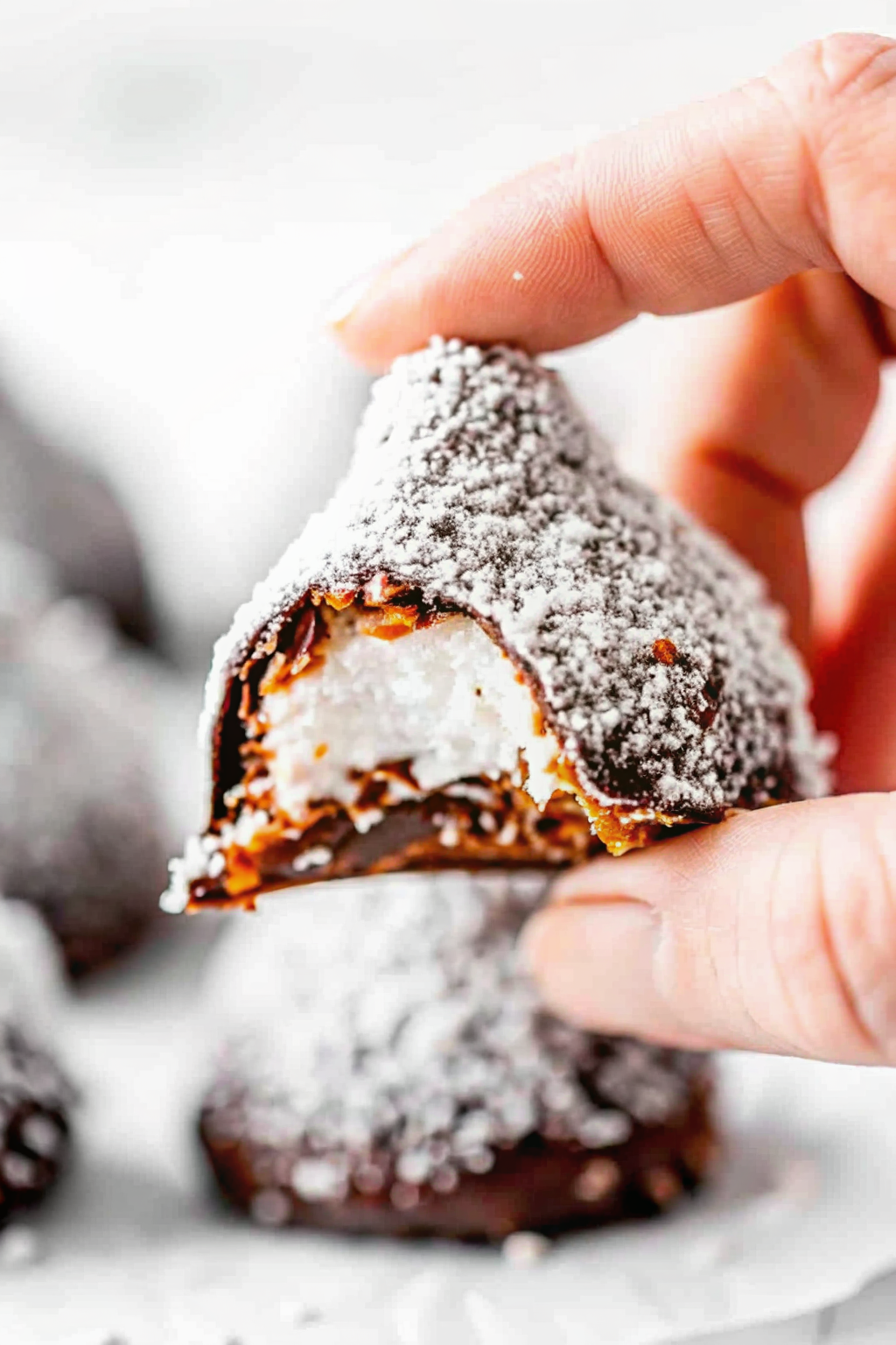 Dipping a marshmallow into melted white chocolate before rolling in coconut
