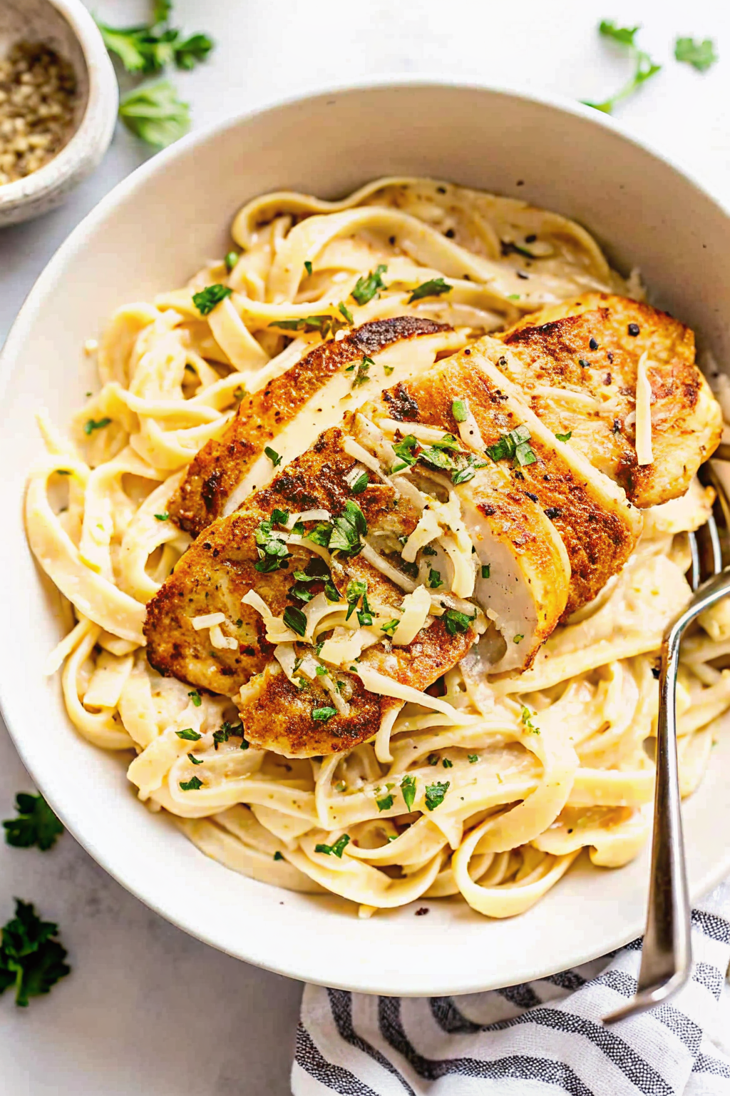 A wire whisk stirring creamy white Alfredo sauce in a pan
