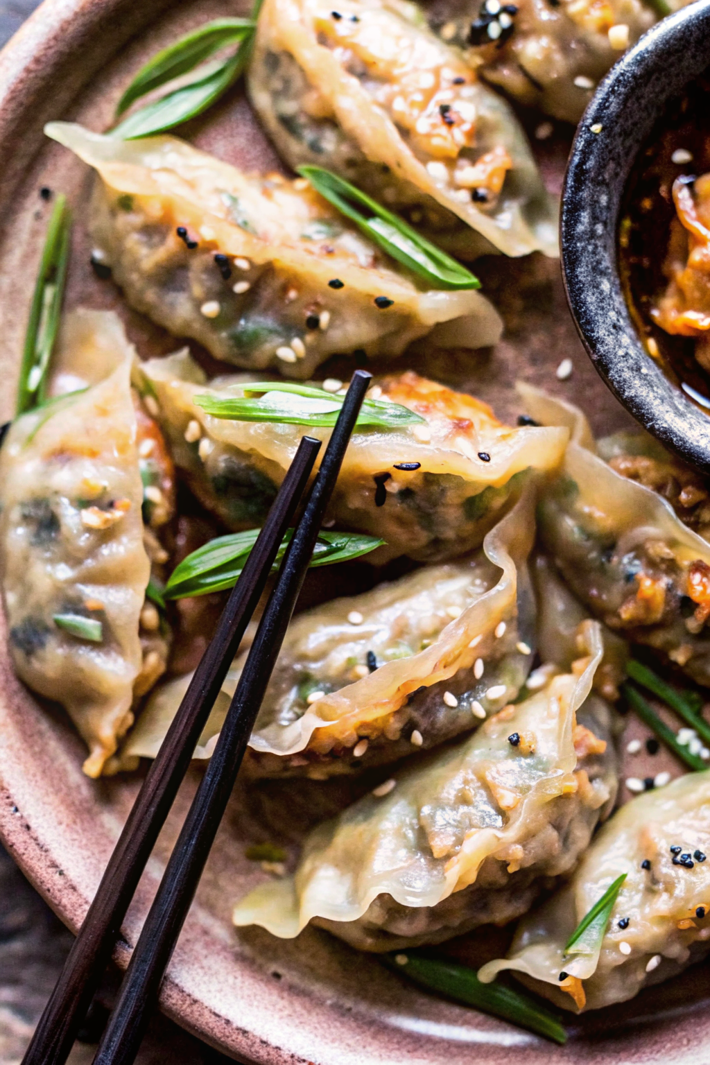 Golden-brown potstickers arranged in a circular pattern on a beige speckled plate with colorful vegetables and savory sauce, featuring Potsticker Stir Fry.